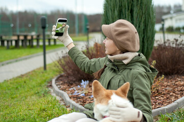 Woman walks with her dog welsh corgi in park. Stylish lady enjoys playtime whith her pet. Takes a photo of her dog.  Fall time.