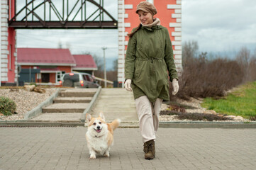 Woman walks with her dog welsh corgi in park. Stylish lady enjoys playtime whith her pet. Autumn season. Fall time.
