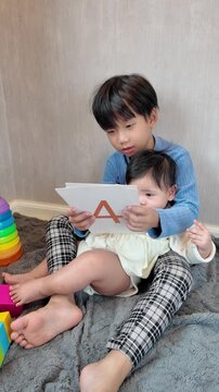 An older brother showing number flashcards to his little sister in the living room, supporting early learning and playful development
