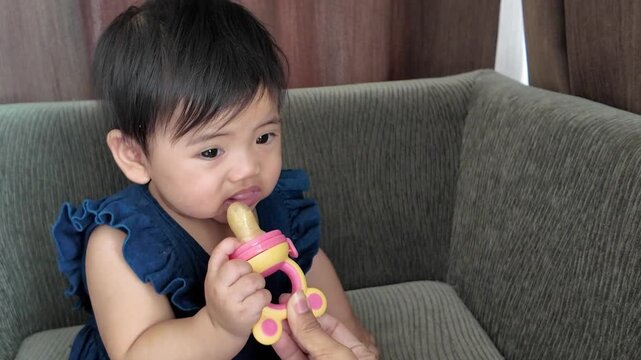 Mother giving her little baby nibbler with food on sofa at home
