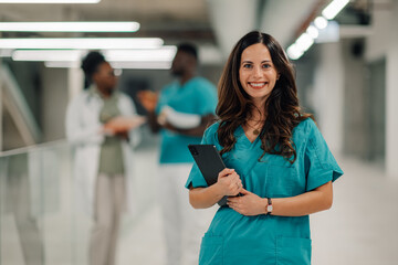 Healthcare professional smiling holding tablet in hospital