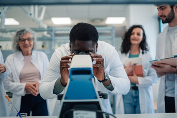 Scientist looking through microscope surrounded by diverse colleagues