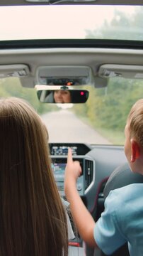 Family idyll concept where lovely happy brother and sister sitting at the rear seat of the auto,watch the way they are driving on and tell stories to their mom who's behind the wheel