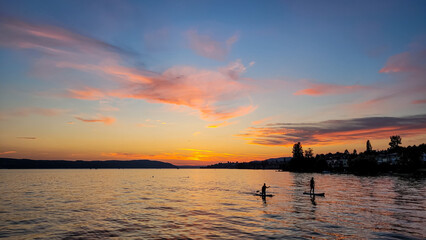 Silhouettes of two people on Stand Up Paddle Board. Sunset on the lake Constance. Water sports.