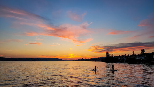 Silhouettes of two people on Stand Up Paddle Board. Sunset on the lake Constance. Water sports.