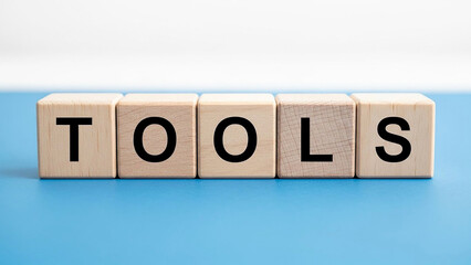 Wooden blocks spelling tools on a blue surface with a white background in a studio setting