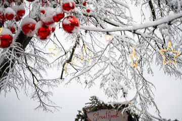 Red Christmas baubles and illuminated stars hang from wintery snow-covered branches above the &ldquo;Streetfood&rdquo; Christmas market hut. Constance, Baden W&uuml;rttemberg, Germany.