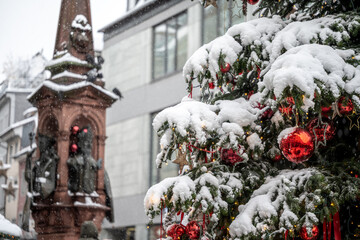 Close-up of a beautifully decorated Christmas tree with red baubles in the market square, which is covered in snow. The fountain is in the background. Constance, Baden W&uuml;rttemberg, Germany.