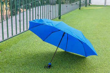 Bright blue umbrella resting on green grass near a fence