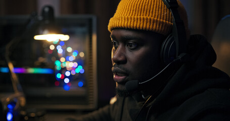 In a dark room filled with purple light, a man with a headset enjoys watching online content. He...