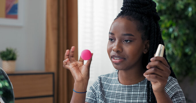 Woman teaches live makeup class for followers. Blogger gives foundation application tips, demonstrating with sponge close to the camera, showing smooth blending techniques.