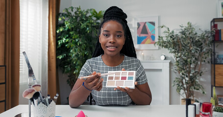 A beauty influencer shows a close-up of her palette. The woman explains color matching tips during a live tutorial, pointing to different vibrant eyeshadow shades.