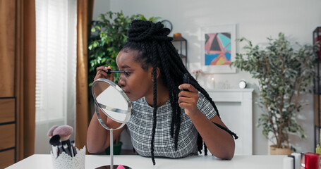 Smiling makeup artist applies mascara while filming a vlog. She looks into the mirror, explaining tips for beautiful lashes, sharing her daily makeup routine with viewers.