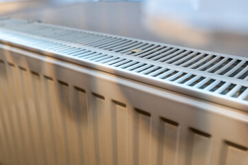 Detailed view of a white radiator in a room, showcasing its design and functionality. Ideal for illustrating home heating systems in interior settings.