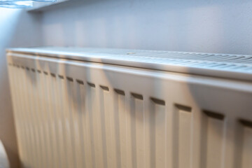 A close-up view of a white radiator with sunlight casting soft shadows on its surface, creating a warm atmosphere in a cozy indoor space, ideal for home comfort.