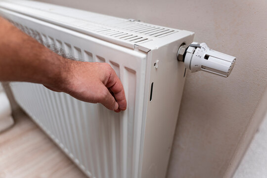 A man adjusting the thermostat of a white radiator in a home setting. The scene conveys warmth and comfort, reflecting a typical household heating situation.