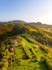 Aerial view of a small hillside farmhouse on a hill near Monte Venda mountain in the Colli Euganei hills with setting sun casting warm light on the hillside near rows of grapevines