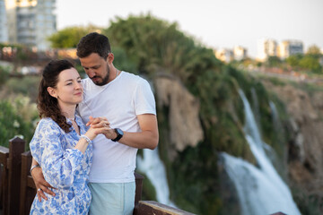 Obraz premium Couple Enjoying a Joyful Moment Together Near a Stunning Waterfall in Antalya, Turkey During Sunset With City Skyline in the Background