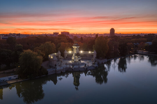 Aerial view of the Monument to Alfonso XII reflecting in the tranquil lake at dusk, set against the vibrant sunset hues painting the Madrid skyline, Madrid, Community of Madrid, Spain.
