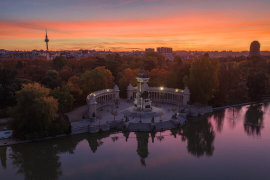 Aerial view of the Monument to Alfonso XII stands majestically in El Retiro Park, its reflection shimmering in the lake under a fiery sunset sky, Madrid, Community of Madrid, Spain.