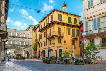 Medieval street in Verona old town with outdoor cafe, colorful building facades and ancient Roman gate Porta Borsari, Veneto, Italy. Italian architecture. Travel and touristic landmark in Europe
