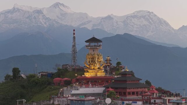 Aerial view of the radiant golden Ganesh statue and pagoda-style structures set against a backdrop of majestic snow-capped mountains, Sarangkot, Gandaki Province, Nepal.