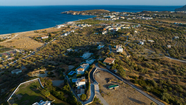 Aerial view of sun-kissed villas nestled amidst the rugged, earthy terrain meeting the turquoise sea, Kolympia, Rhodes, Greece.