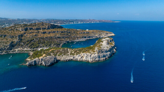 Aerial view of boats cutting through the deep blue sea surrounding the rocky coastline of Faliraki, Rhodes, Greece.