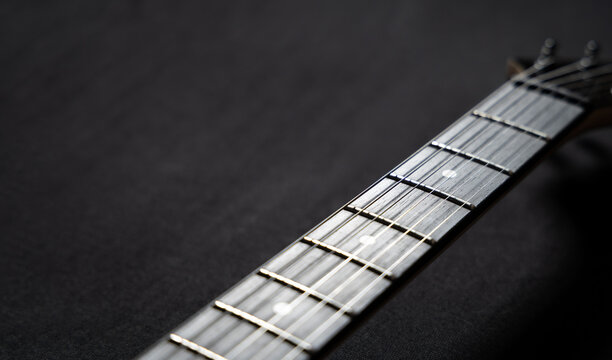 Close-up of an electric guitar neck and headstock on a black background. Musical instrument concept highlighting strings, tuning pegs, craftsmanship, and modern music culture.