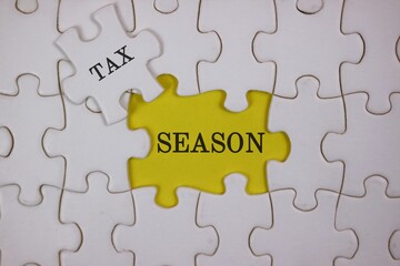 Fototapeta premium Close-up of puzzle pieces, featuring a yellow piece labeled SEASON beside a white piece labeled TAX. Symbolizes the link between tax season and personal or business finances.