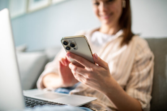 Young adult woman smiling, using smartphone at home