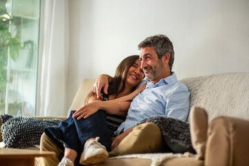Affectionate couple hugging and smiling while relaxing on cozy living room couch