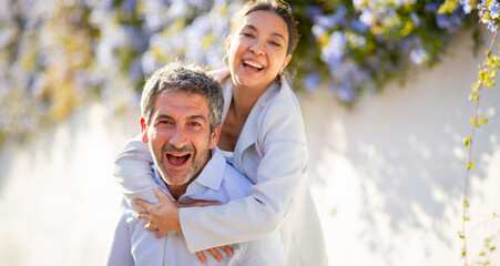 Laughing couple in playful piggyback moment surrounded by flowers