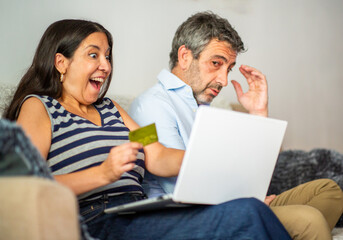 Excited woman and worried man shopping online with laptop and credit card