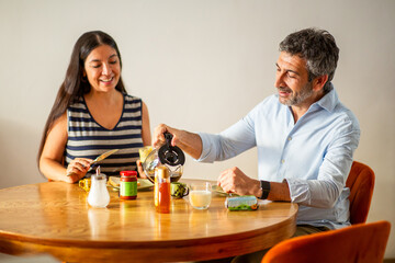 Smiling couple enjoying breakfast together while pouring coffee and preparing toast