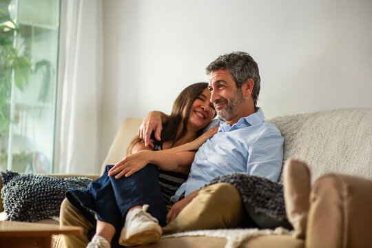 Affectionate couple hugging and smiling while relaxing on cozy living room couch