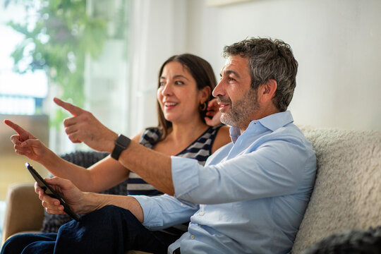 Happy couple pointing at television while watching together on sofa at home