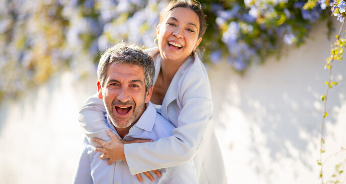 Laughing couple in playful piggyback moment surrounded by flowers