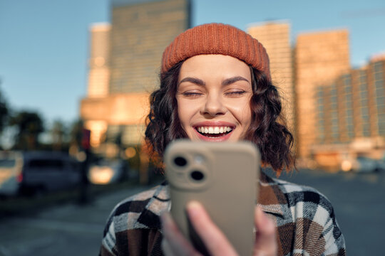 Woman smile smartphone urban beanie curlyhair golden candid young woman laughing at phone in city at golden hour glow, authenticity and mindful living vibe with emotional storytelling. - Powered by Adobe