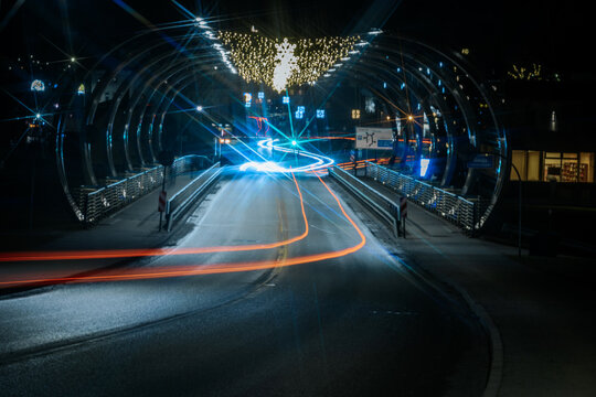 Nighttime urban bridge illuminated with festive lights, showcasing vibrant light trails from passing vehicles, creating a dynamic and lively atmosphere in the city