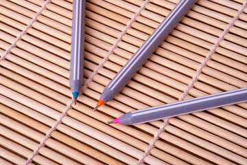 Three precision fine-tip pens with colorful tips rest on a woven bamboo mat. Representing essential tools for creative writing, meticulous work and high-level education. Perfect for website design.