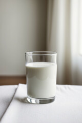 A glass of milk, placed on a white tablecloth, with a soft natural illuminating the scene and a blurred background of a modern kitchen 