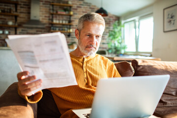 Senior man worried reviewing bills on laptop at home