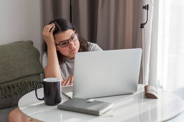 Tired woman working from home with a laptop, feeling stressed and overwhelmed during remote work. Natural daylight, casual home environment, productivity struggle and fatigue concept.