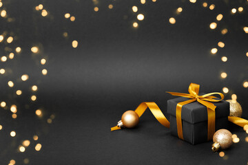 Black gift box with golden ribbon bow on black background