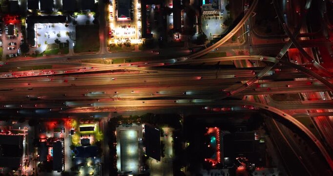 Illuminated road interchange with multiple cars moving by. Flow of cars going by the motorways and trestles at night. Aerial view.