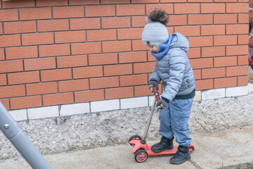 Young kid boy riding on a small kick scooter alone outdoors. Childhood activity, leisure time, and development concept for children.