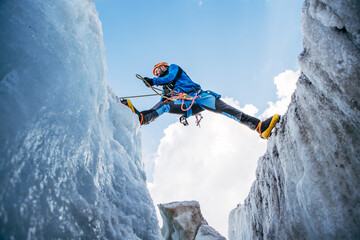 Wide-angle shot of Climber vibrant gear overcomes over crevasse on icy glacier during Lenin peak ascent with clear sky in background. Extreme active people high-altitude mountaineering concept image