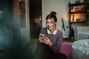 Young woman relaxing at home using smartphone and headphones