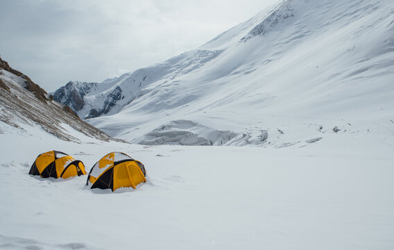 Camp 2 at 5300m. Bright tents stand on snowy Lenin Glacier with vast panoramic view frying pan and Pamir mountains slopes. Active people concept. Lenin peak expedition route in Kyrgyzstan Central Asia